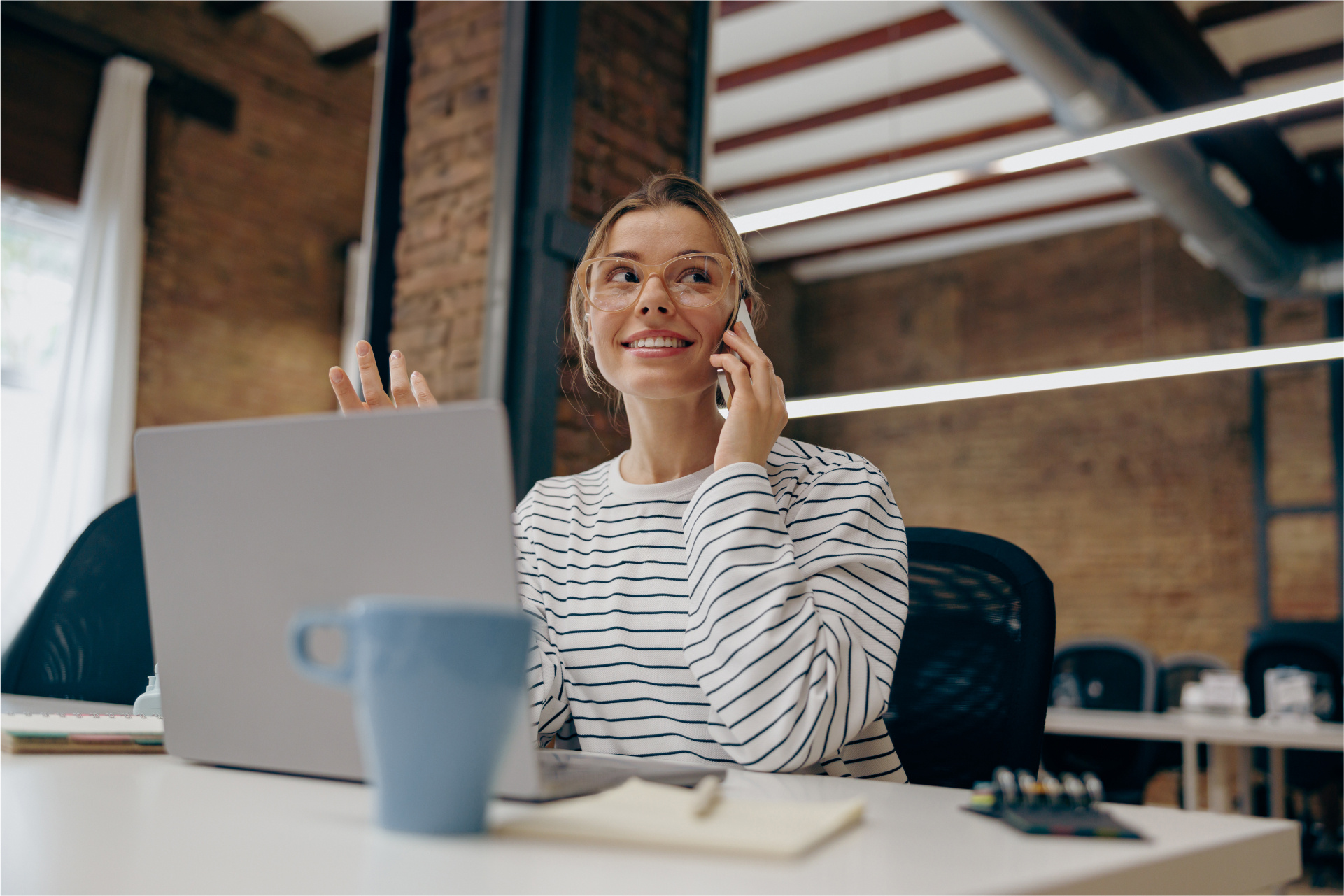 smiling-female-entrepreneur-working-laptop-while-sitting-office-talking-by-phone (1) 1